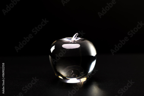 Fotografie A clear glass apple paperweight sits on a dark surface against a black background