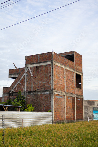 Unfinished brick building under construction with natural light, surrounded by green field and clear sky, providing copy space for real estate development projects
