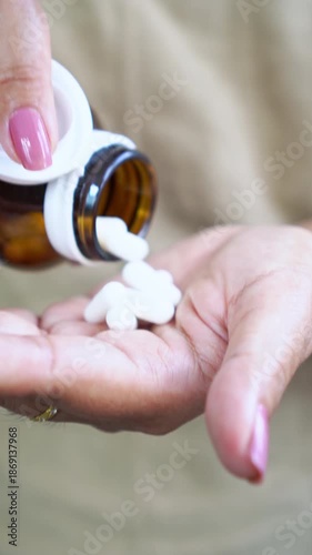Vertical close up of a woman's hand holding a medicine bottle while taking vitamin pills and supplements like probiotics or magnesium to support her daily health, wellness, and medical wellbeing
