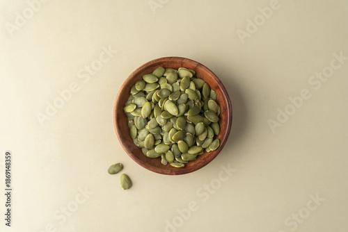 Green Pumpkin seeds in a wooden bowl placed on a beige background.