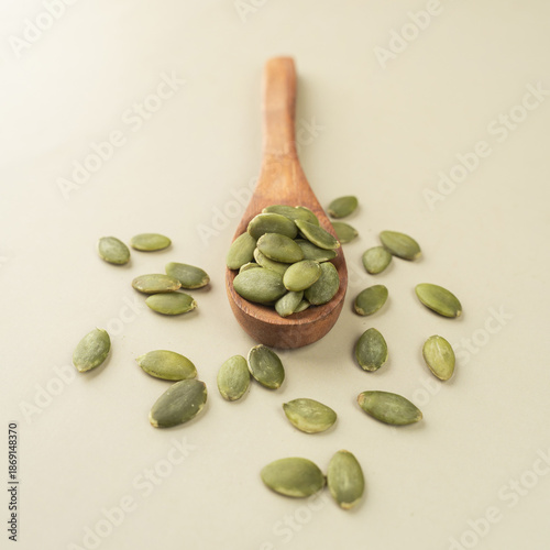 Green Pumpkin seeds in a wooden spoon placed on a beige background.