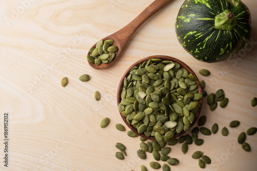 Green Pumpkin seeds in a wooden bowl, along with green baby pumpkin, placed on a textured background.