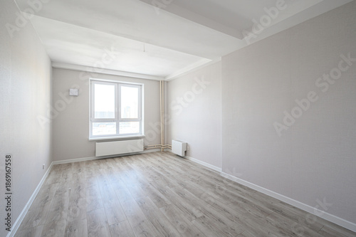 bright, empty room with light grey laminate flooring, off-white walls, large double window, white radiator, minimal fixtures, clean and airy atmosphere
