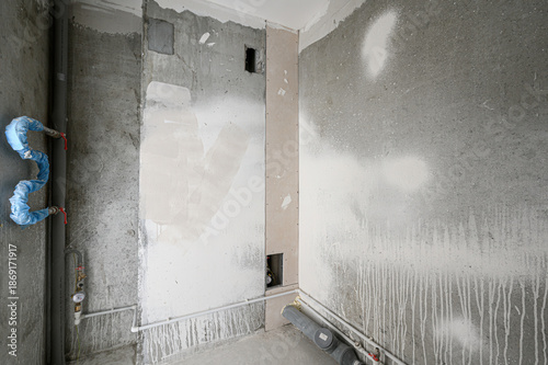 Fotografie room in rough condition with unfinished concrete walls, exposed plumbing pipes, partially plastered areas