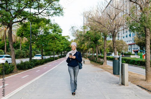 Wallpaper Mural Woman wearing hijab walking in city park using phone Torontodigital.ca