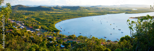 Sunlit river bend backed by mangroves and scattered hillside homes.