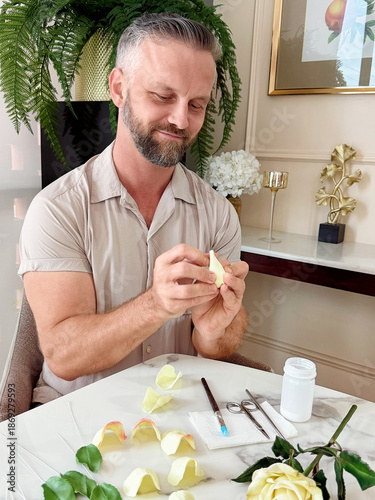 Bright conceptual photo of a muscular bearded man painting, gluing and assembling a flower made of air dry clay. Creative handmade process and art workshop concept, Vertical, focus on men