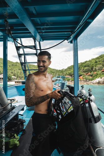 Tattooed male scuba diver preparing diving equipment on a boat in tropical island