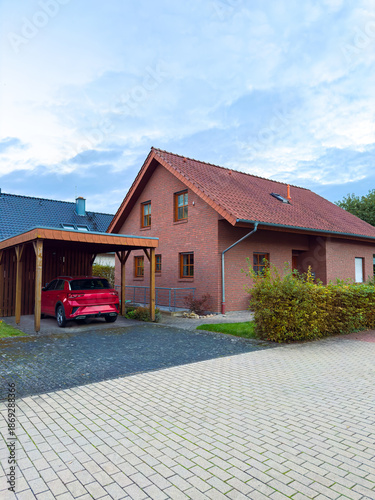 Photos House with a red car parked in a carport in a residential area during early even