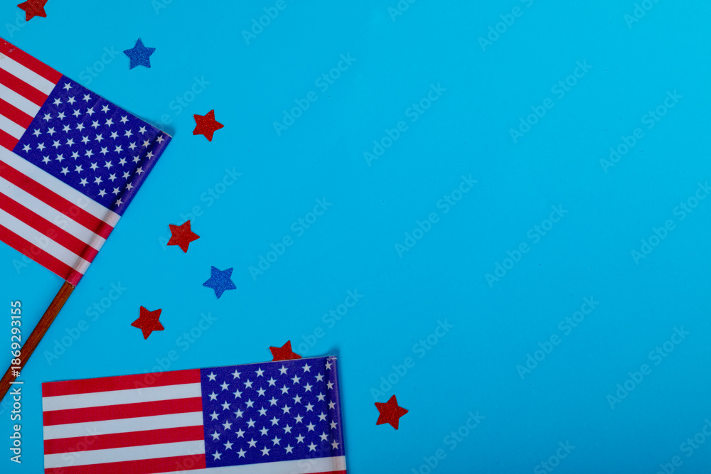 Fototapeta premium Overhead view of small america flags on sticks by glitter stars by copy space over blue background