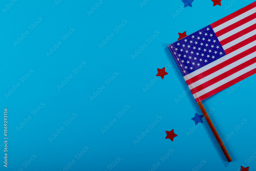 Fototapeta premium Overhead view of small america flag on stick by glitter stars by copy space over blue background