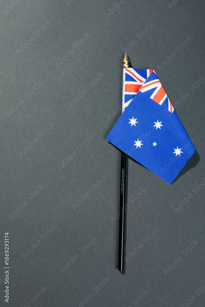 Fototapeta premium Overhead view of stars and union jack on australia flag stick by copy space over black table