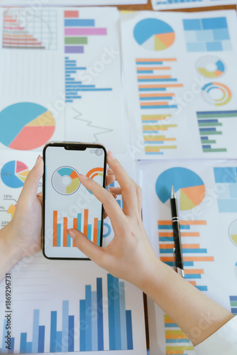 A close-up image shows an Asian businesswoman and accountant analyzing financial data in her office using a smartphone and laptop. (Finance, Business, Tax, Accounting)