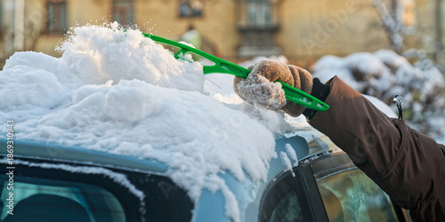 Person sweeping fresh white snow off a blue automobile windshield and top after a blizzard. Seasonal morning routine and cold weather care. Photo