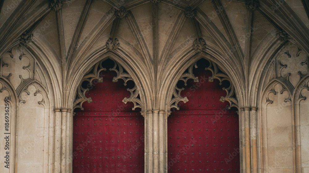 Fototapeta premium Gothic arched doors with red wooden panels and stone vaults