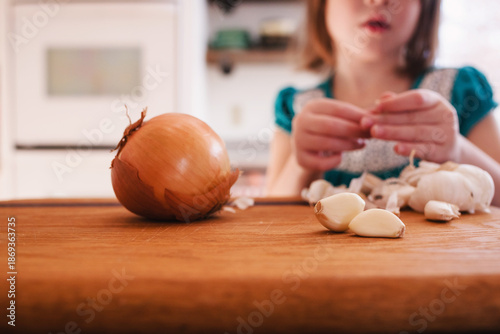 Close-up of a Young Girl standing in a kitchen peeling a stack of garlic gloves 