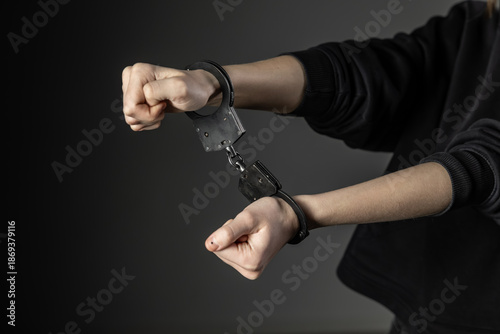 Obraz na plátně A close-up of a person’s wrists locked in black handcuffs, set against a dark background