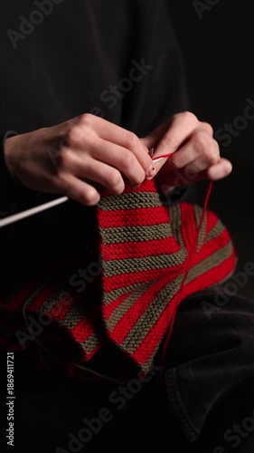 Wallpaper Mural Close-up of a person knitting a red and green striped fabric with needles, seated against a dark background. Focus on yarn and hand movement. Copy space Torontodigital.ca