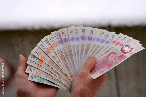 Close-up of man holding fan of Englisch Pound banknotes outdoors at terrace on a snowy winter day. Photo taken January 8th, 2026, Zurich, Switzerland.