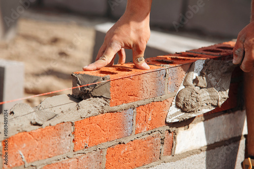 Photos Close-up of Bricklayer constructing brick wall using red bricks, cement and tool