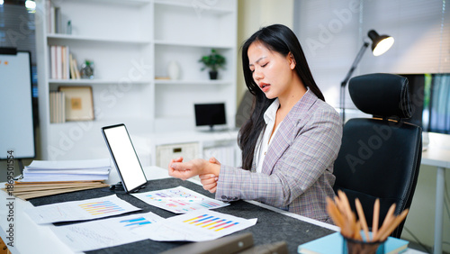 Fotografía Young Asian Businesswoman suffering from wrist pain while working on computer, B