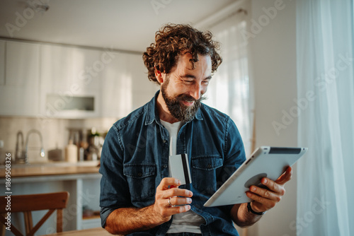 Man happy online shopping using tablet and credit card at home