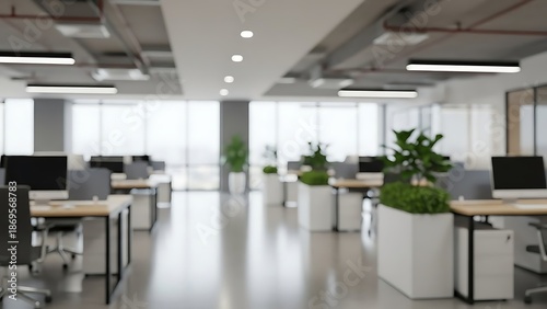 Blurred view of a contemporary office workspace featuring rows of desks and green plants