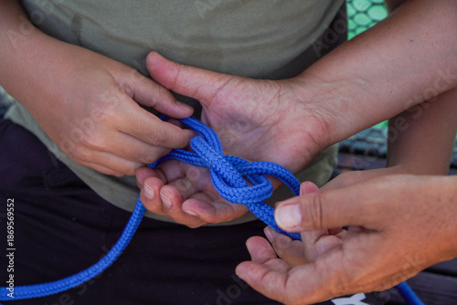 Fotografia A close-up of hands tying a knot with bright blue rope