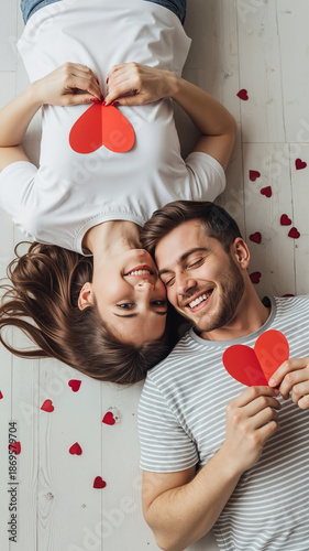 Young couple lying together and holding red hearts on floor  