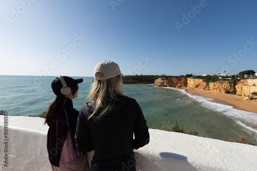 A mother and daughter enjoying the beautiful view Yellow rocks and cliffs on the sandy beach. A cove by the sea, Our Lady of the Rock, Praia Nova, Lagos. Algarve, Portugal