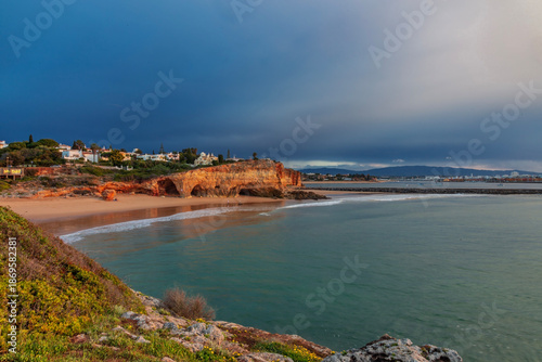 A dramatic and atmospheric view of Praia do Pintadinho in the Algarve, Portugal, captured during the golden hour under a moody, stormy sky.