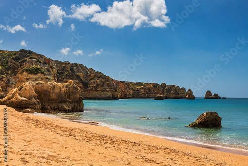 A stunning and iconic view of Praia dos Três Irmãos in the Algarve, Portugal, showcasing its breathtaking golden sand beach framed by towering, dramatic limestone cliffs.