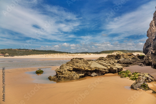 A breathtaking panoramic view of Praia da Amoreira in the Algarve, Portugal, showcasing its vast expanse of golden sand stretching toward distant dunes and lush green hills
