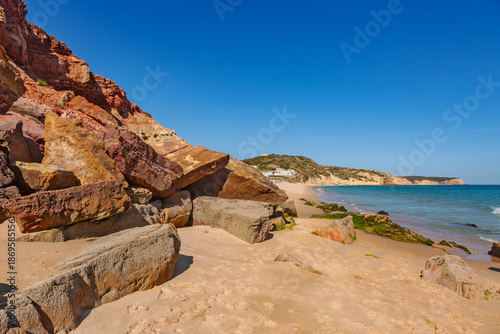 A stunning view of Praia da Salema in the Algarve, Portugal, where golden sands meet the turquoise waters of the Atlantic Ocean under a brilliant blue sky.