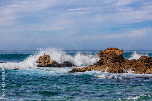 Powerful Atlantic waves explode in a burst of white spray as they crash against the weathered rock formations of Praia do Castelejo in the Algarve, Portugal.