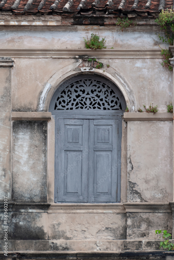Fototapeta premium Antique Wooden Window with Ornate Carving on Weathered Stucco Wall
