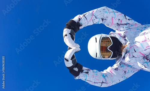 A cheerful skier posing under a bright blue sky, making a heart gesture with hands as a symbol of winter sports enjoyment