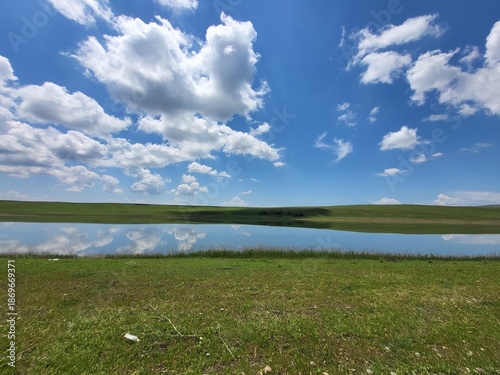 Foto “Mirror-like lake reflecting clouds on a sunny summer day”