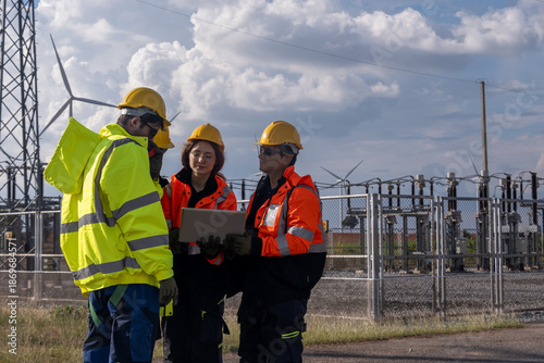 Team of workers discussing project at wind farm site in afternoon sunlight