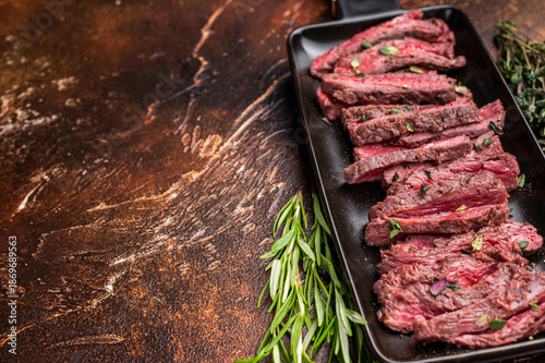 Fotografi BBQ Grilled Flank beef steak, sliced meat with herbs, brown background