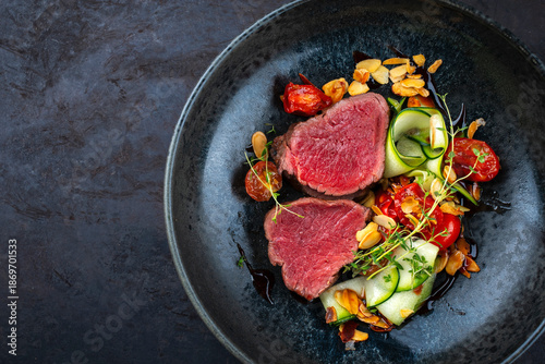Fine dining dry aged beef filet steak rare tataki style cut tagliata with sliced zucchini, tomato and almonds
