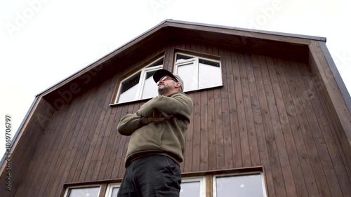 An adult man stands in front of a wooden house. Communication. Business. Nature.