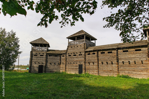 Photography Historic wooden fortress with log walls and watchtowers, standing in a green landscape, representing medieval defense architecture and cultural heritage