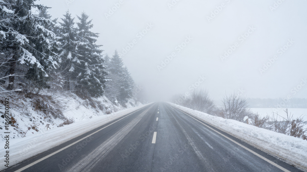 Fototapeta premium Empty snow covered highway stretching into the distance during a foggy winter day