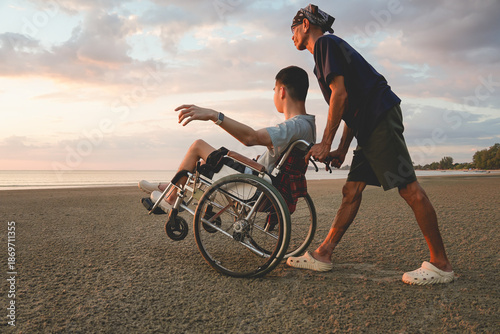 Schilderij op canvas Asian elderly caregiver pushing wheelchair with disabled family member at the beach during sunset