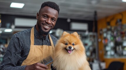 Joyful Black groomer in apron with comb beside Pomeranian at pet grooming shop stock photo