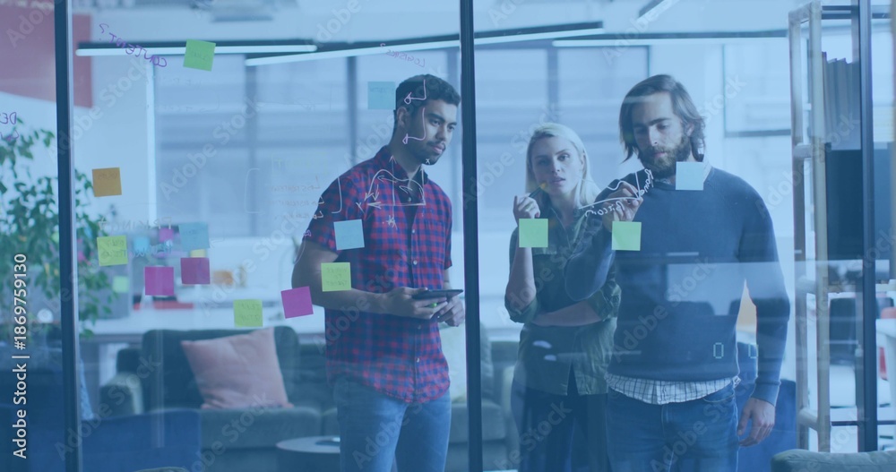 Fototapeta premium Collaborating team reviewing sticky notes and marker sketches on glass wall at lounge, with tablet