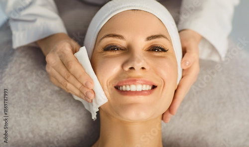 Bild auf Leinwand Portrait of a happy smiling young pretty woman client looking cheerful at camera while lying in spa salon having a face treatment and receiving beauty procedure from beautician in beauty clinic