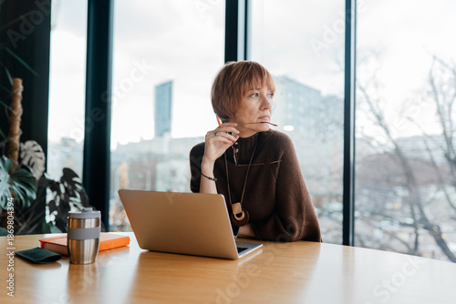 Billede på lærred White woman aged 40 looking away while working on laptop at office table