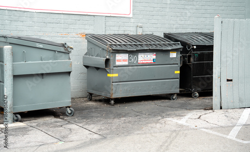 Foto Commercial dumpsters lined up against a brick wall in an urban alleyway setting